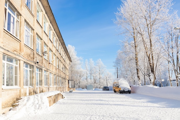 Casa de três andares com quintal coberto de neve e árvores estacionadas automóveis dia ensolarado de inverno