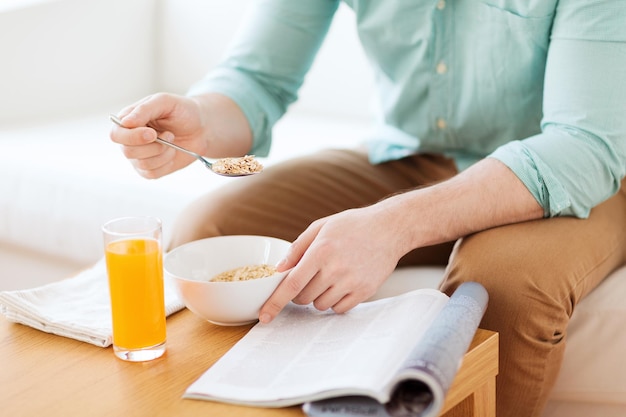 Casa, descanso, notícias, café da manhã e conceito de pessoas - close-up do homem lendo revista e tomando café da manhã em casa