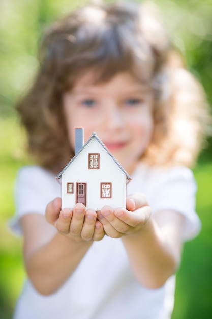 Casa de ecología en manos de los niños contra el fondo verde primavera