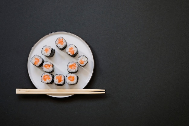 Casa em forma de rolos de sushi com pauzinhos em fundo preto, com espaço de cópia