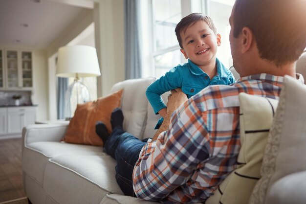 Casa feliz y padre con hijo en el sofá para vincularse riendo y relajándose juntos el fin de semana Familia jugando y padre con niño pequeño en el sofa para la relación lúdica amor y diversión en la sala de estar