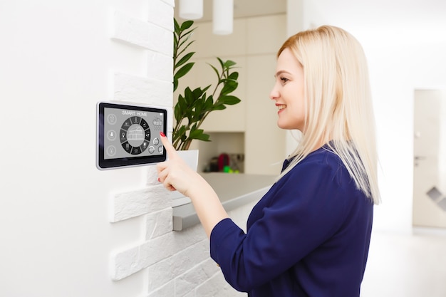 Casa inteligente. Mulher bonita e alegre olhando para o painel sensorial enquanto o pressiona