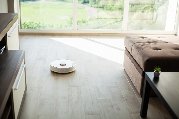 Casa inteligente. El robot aspirador funciona en el piso de madera en una sala de estar.