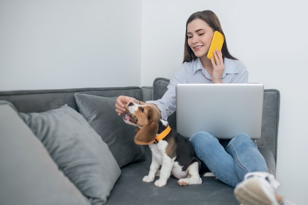 En casa. Joven morena trabajando en un portátil y jugando con un cachorro