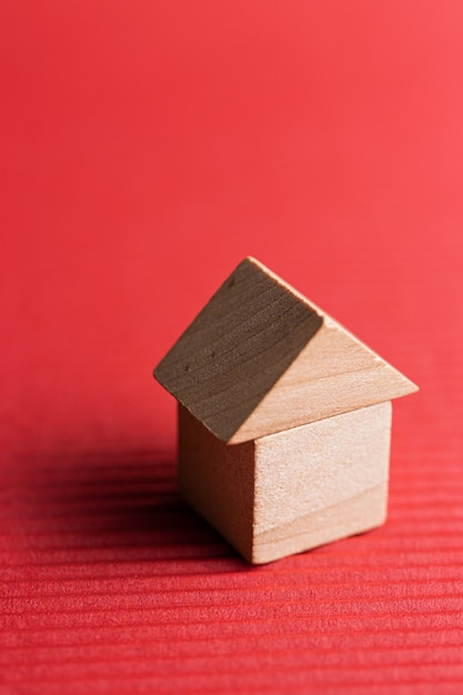 Casa de juguete de bloque de madera sobre una superficie roja. Imagen conceptual de adquisición de vivienda. Copia espacio