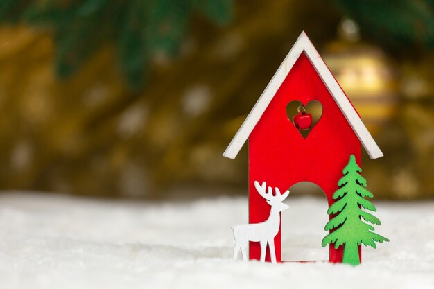 Casa de juguete de madera de Navidad, ciervos y árboles sobre una manta blanca imitando la nieve.