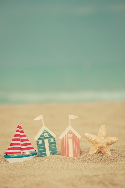 Casa de juguete en la playa de arena contra el mar azul