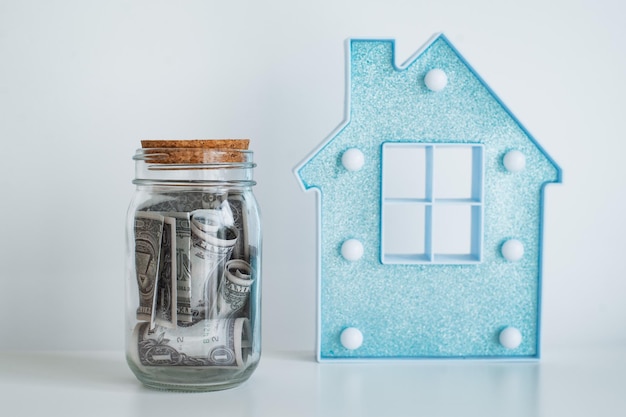 Casa de la lámpara con un frasco de billetes de un dólar sobre una mesa blanca