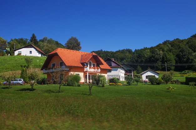 Casa laranja campo da Europa entre a exuberante paisagem verde verão e céu azul