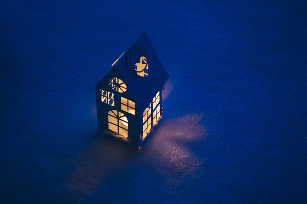 Casa de linterna con vela encendida sobre la nieve por la noche.