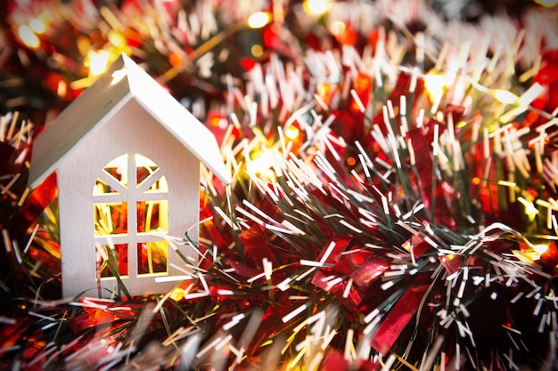 Casa de madera blanca con adornos navideños, oropel rojo y guirnaldas de luces doradas. Año nuevo, confort, calidez hogareña, acogedor. Fondo de Navidad. Copia espacio