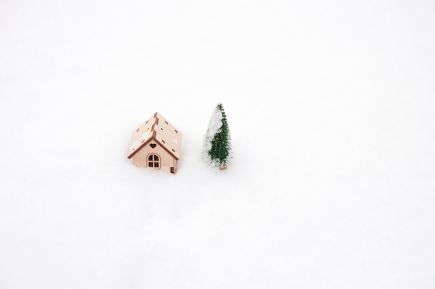 Casa de madera de juguete y árbol de Navidad en la nieve.