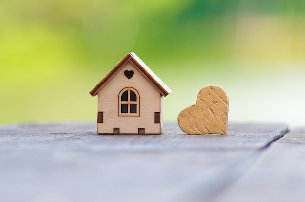 Una casa de madera de juguete se encuentra junto a un corazón de oro sobre una mesa de madera