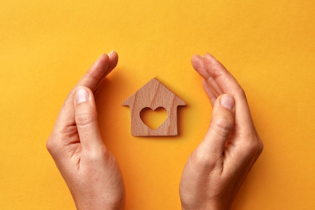 Una casa de madera en manos de un hombre. Un símbolo de protección y cuidado del hogar y la familia.