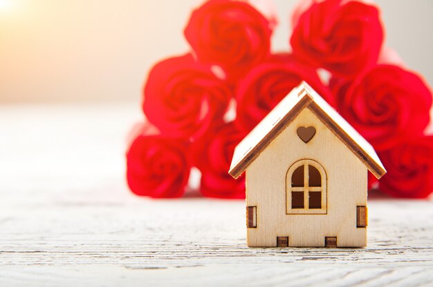 Casa de madera en miniatura sobre un fondo de rosas. Concepto de regalo de primavera.