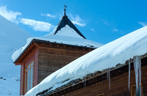 Casa de madera (con nieve y carámbanos en el techo) en la ladera de la montaña de invierno.