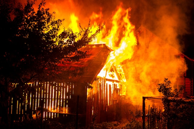 Casa de madera o granero ardiendo en llamas por la noche.