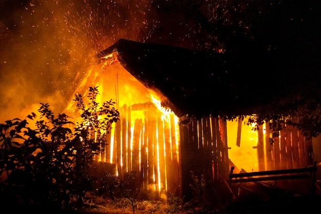 Casa de madera o granero ardiendo en llamas por la noche.