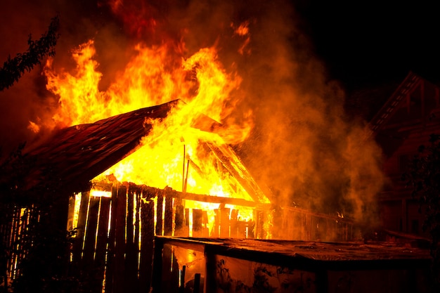 Casa de madera o granero ardiendo en llamas por la noche.