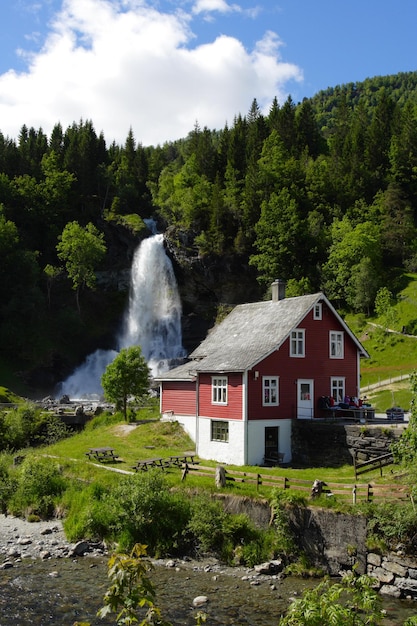 Casa de madera tradicional noruega con cascada en la distancia