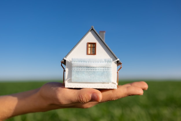 Casa con máscara protectora en la mano contra el campo verde de primavera y la superficie del cielo azul