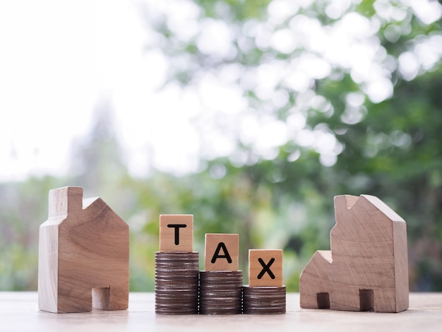Casa en miniatura y bloques de madera con la palabra TAX en la pila de monedas El concepto de pago de impuestos para la casa Inversión inmobiliaria Hipoteca de la casa Inmobiliaria