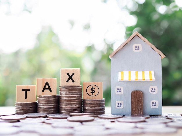 Casa en miniatura Bloques de madera con la palabra TAX y pila de monedas El concepto de pago de impuestos para la casa Inversión inmobiliaria Hipoteca de la casa Inmobiliaria