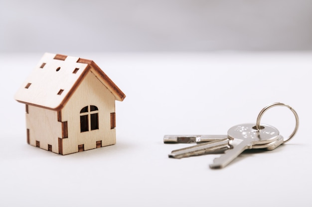 La casa miniatura de madera con llaves de la puerta se cierra para arriba. Concepto de bienes raíces Casita de madera de juguete con llaves con copia espacio.