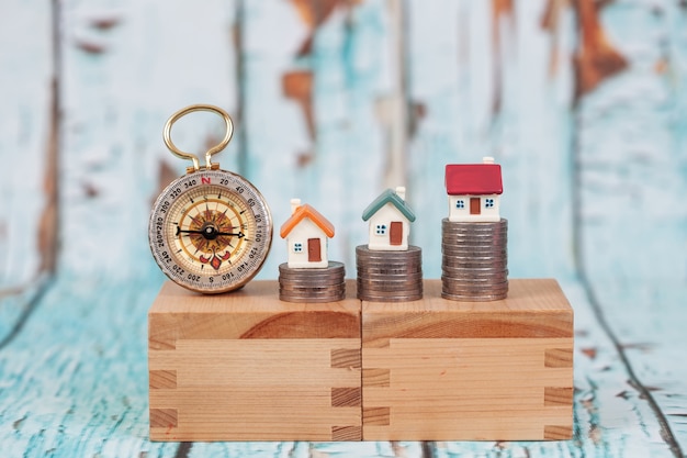 Foto casa en miniatura en la pila de monedas en el soporte de madera con pared de madera.