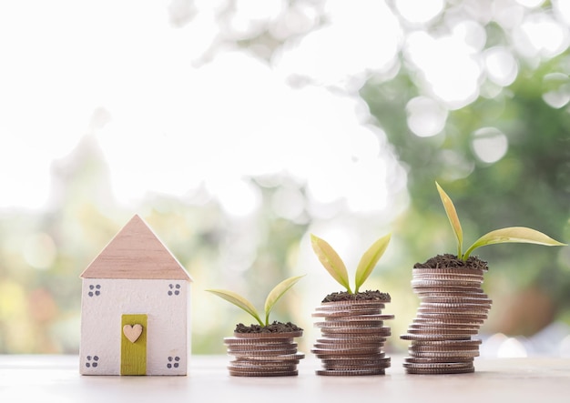 Casa en miniatura y plantas que crecen en una pila de monedas El concepto de ahorrar dinero para la casa Inversión inmobiliaria Hipoteca de la casa Inmobiliaria