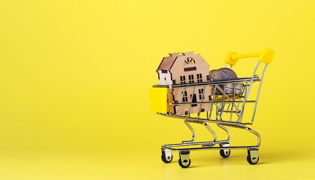 Foto casa modelo e moedas no mini carrinho de compras em fundo amarelo