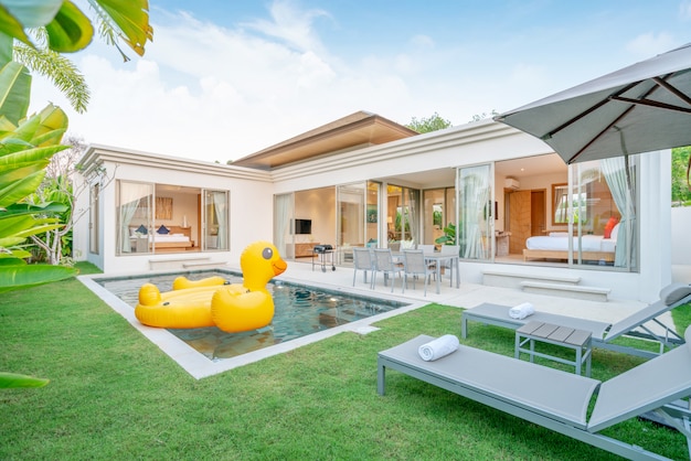 Foto casa o casa. diseño exterior que muestra una villa con piscina tropical con zonas verdes, tumbonas y pato flotante.