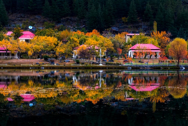 Una casa a la orilla de un lago con techo rojo y árboles al fondo.