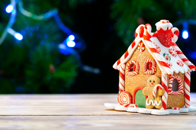 Casa de pan de jengibre en una mesa de madera contra la de un árbol de Navidad.