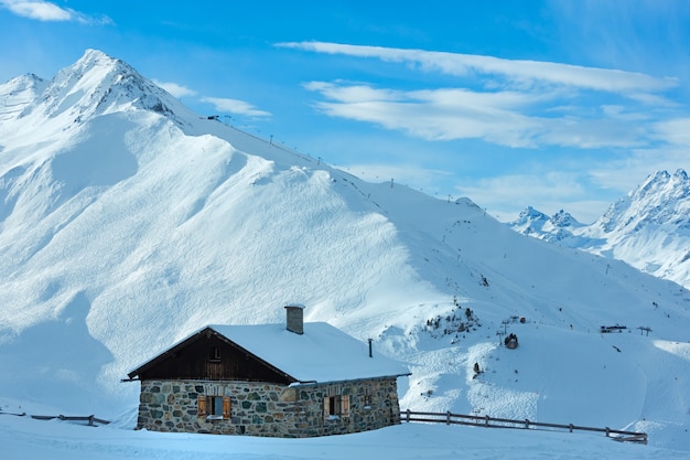 Casa pedregosa y pista de esquí en la ladera nevada de la montaña del invierno (Tirol, Austria). Todas las personas son irreconocibles.