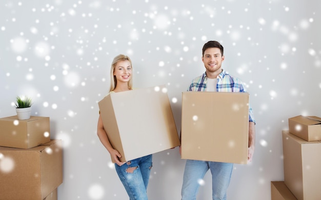 Foto casa, pessoas, reparação e conceito imobiliário - casal sorridente com grandes caixas de papelão, movendo-se para um novo lugar sobre a neve