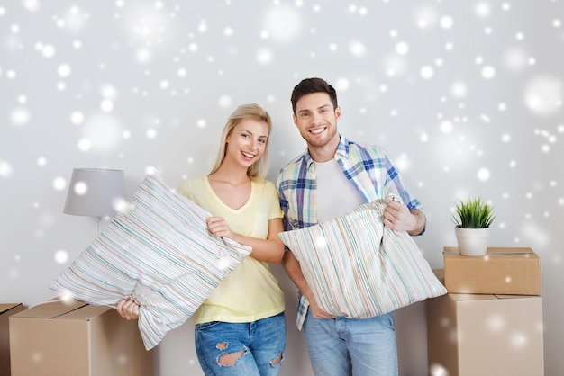 casa, pessoas, reparo e conceito imobiliário - casal sorridente com grandes caixas de papelão, almofadas e outras coisas se mudando para um novo lugar sobre a neve