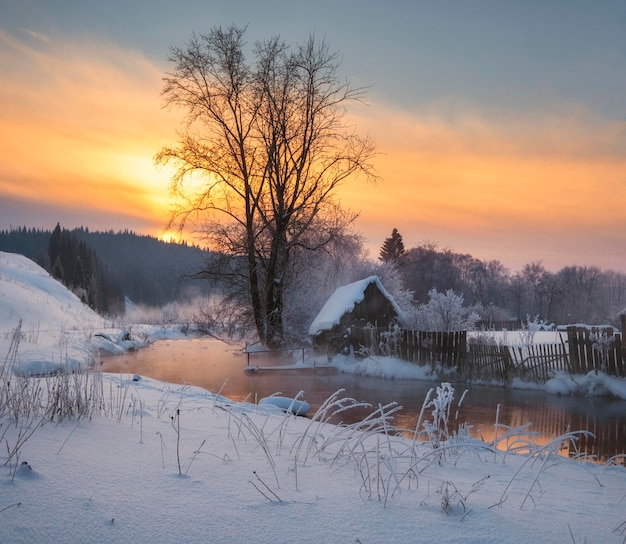 Casa en el pueblo cerca del río con el telón de fondo de las montañas en una noche de invierno al atardecer