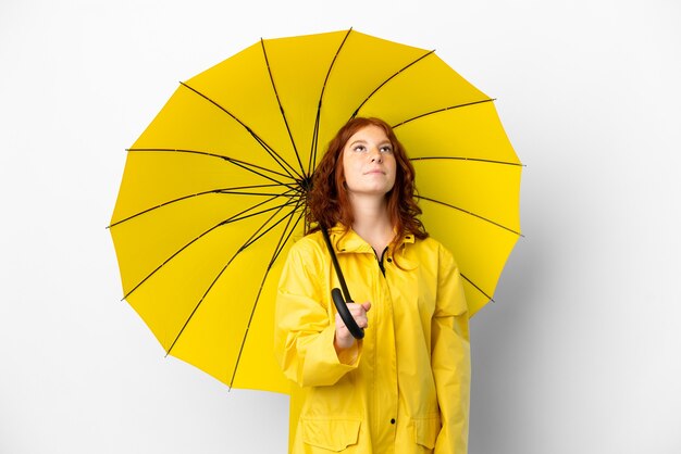 Casaco à prova de chuva de menina ruiva adolescente e guarda-chuva isolado no fundo branco e olhando para cima