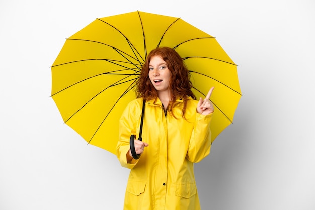 Casaco à prova de chuva e guarda-chuva adolescente ruiva isolado no fundo branco com a intenção de perceber a solução enquanto levanta um dedo