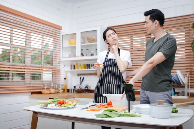 Casais asiáticos têm o prazer de cozinhar na cozinha de casa