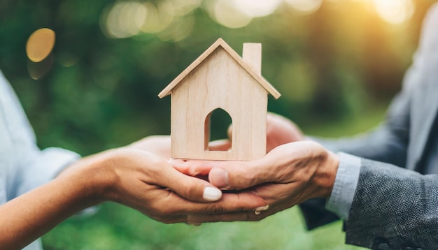 Casais casados com as mãos segurando uma casa de madeira simbolizando a propriedade da casa e as aspirações imobiliárias