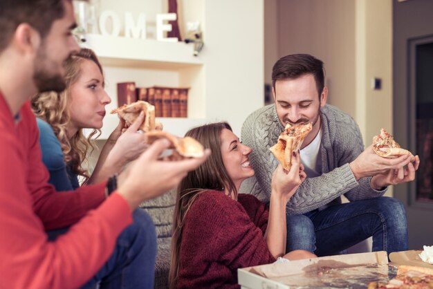 Casais jovens comendo pizza na sala de estar