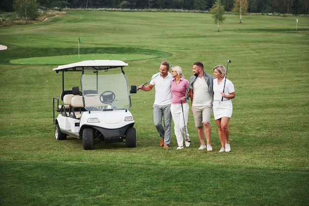 Casais jovens se preparando para jogar. Um grupo de amigos sorridentes chegou ao buraco em um carrinho de golfe