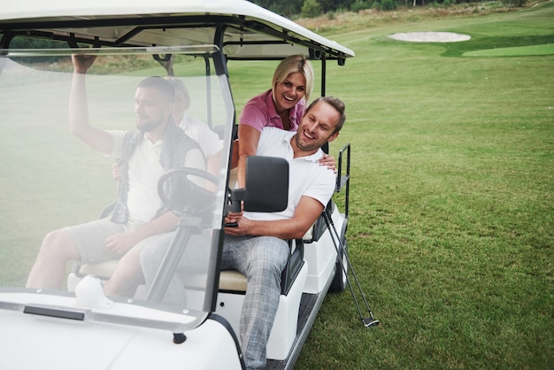 Casais jovens se preparando para jogar. um grupo de amigos sorridentes chegou ao buraco em um carrinho de golfe