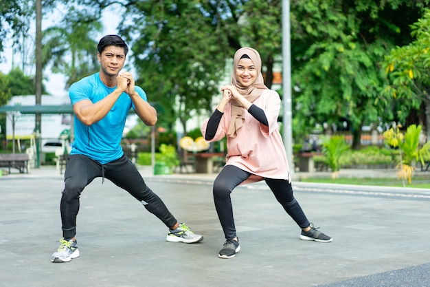 Casais muçulmanos em roupas de ginástica fazendo o aquecimento das pernas juntos antes de se exercitar no parque