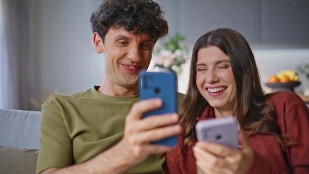 Casal a rir a reagir a um vídeo de telemóvel no sofá da sala de estar em close-up
