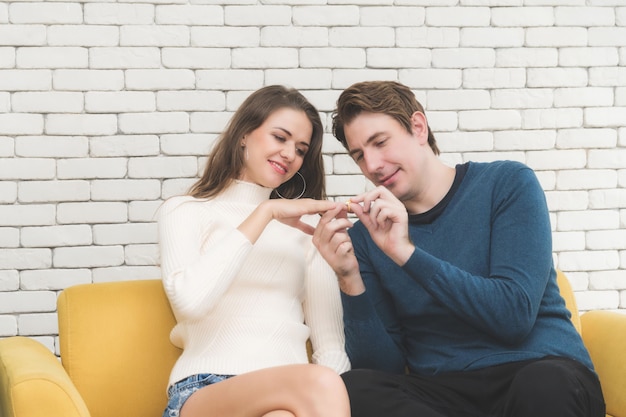 Casal abraçando e segurando as mãos enquanto parece um anel de noivado.