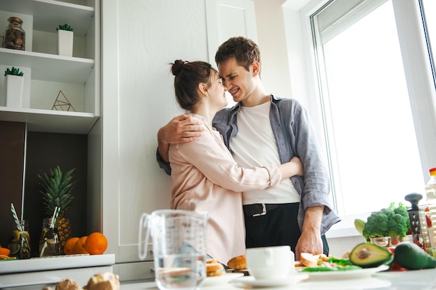 Casal abraçando em pé na cozinha querendo fazer o café da manhã cozinhando juntos cozinha rela