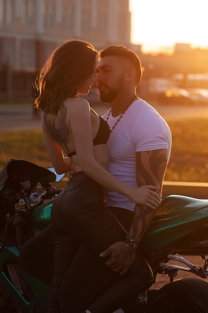 Casal abraçando perto de moto ao pôr do sol